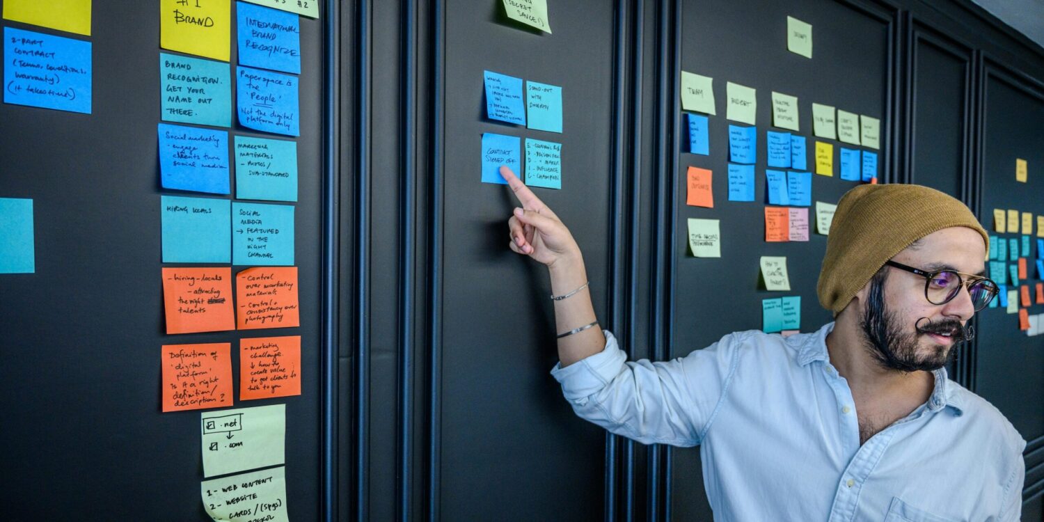 During a brainstorming session, a person wearing a beanie points at sticky notes on the wall, bringing innovative ideas to life with the entrepreneurial spirit akin to that of Omidyar Network.